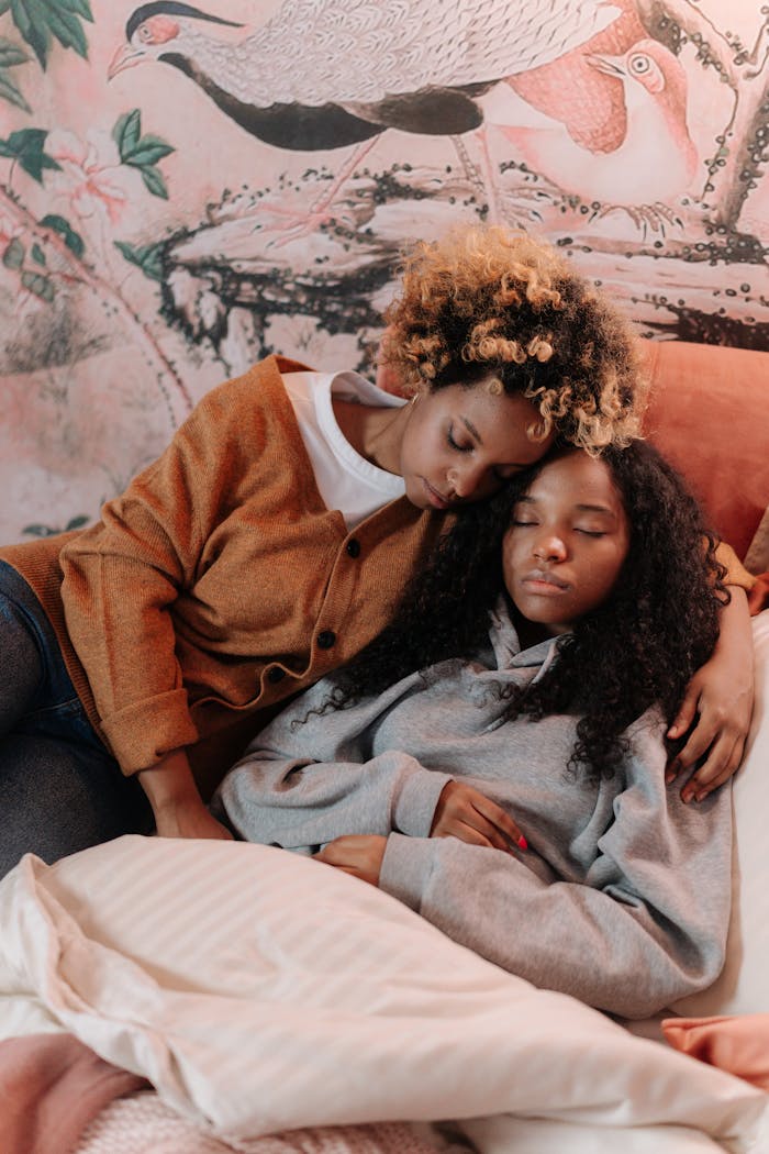 services-01 A loving mother embraces her sleeping daughter on a cozy bed, surrounded by warm decor.